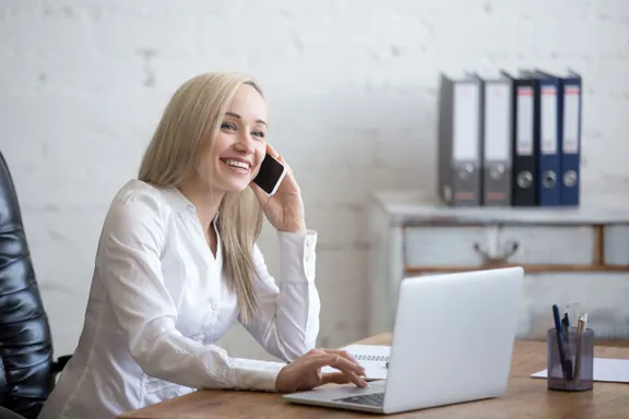 Vrouw belt lachend aan haar bureau